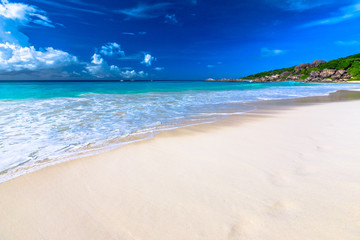 White sandy beach and turquoise clear sea of Grand Anse with copy space in the sand. Peaceful wallpaper of tropical Seychelles beach, La Digue.
