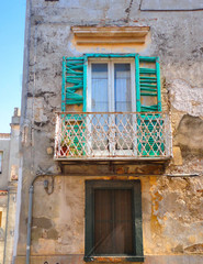 Fototapeta na wymiar South Italy, Venosa Basilicata, Old building with ruined facade with colorful green broken wooden window shutter and vintage iron balcony. 