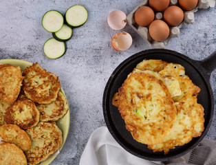 The process of making pancakes from zucchini. on a marble table - a plate with an ornament and dough for pancakes, as well as eggs and a pan with prepared pancakes