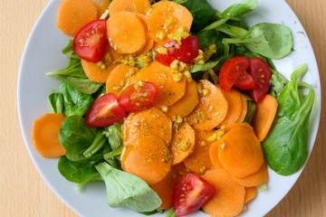 Aerial view of a healthy vegetarian homemade salad with nut lettuce or lamb's lettuce, carrot slices, tomatoes and garlic on a white plate