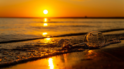 A glass washed by waves on a sandy beach against the background of the sunset.