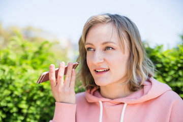 Young woman's portrait listening voice message on smart phone on green trees background