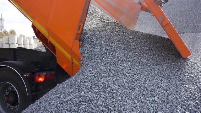 A dump truck is dumping gravel at the excavation site. Stock footage. Close up of unloading process of a construction truck full of small stones.