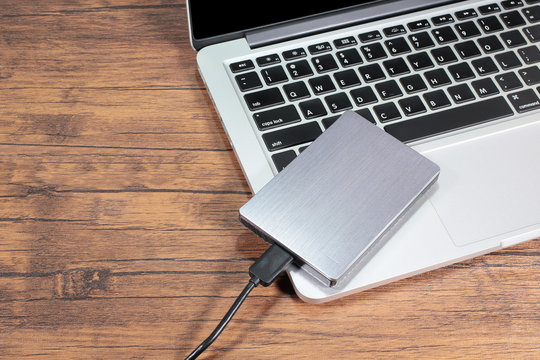 External hard drive connect to laptop computer on wooden background