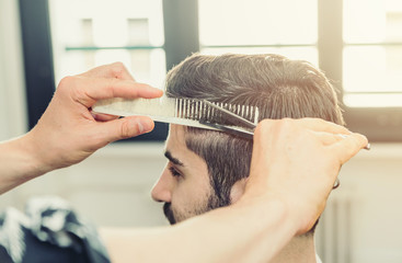 Hairdresser cuts man's hair with comb and scissors