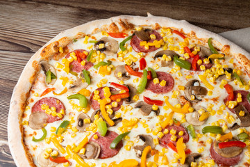 Tasty Italian pizza Mexicano on wooden background. Top view of hot pizza with chili pepper , hot sausages, onion, tomatoes and cheese. Flat lay. Advertising photo for a site or menu.