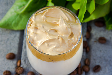 Dalgona coffee and coffee beans on grey concrete background with green branch. Top view.