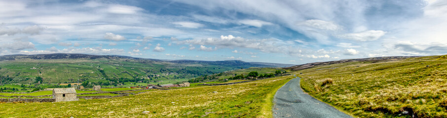 a panorama of hills of the Yorkshire Dales with lone stone building and blue sky with clouds