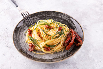 Spaghetti with agretti, a spring vegetable from Italy, and sun dried tomatoes with fork on a black...