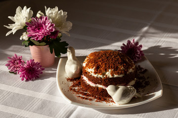 Freshly baked homemade chocolate cake with cream cheese on white plate. Chrysanthemums on the table.