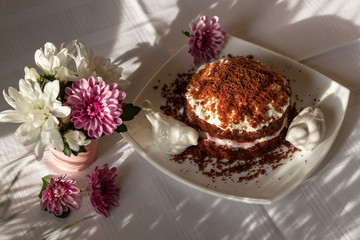 Freshly baked homemade chocolate cake with cream cheese on white plate. Chrysanthemums on the table.