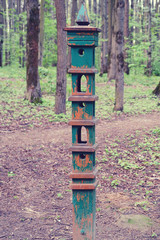Pole with a feeder for birds and squirrels in the forest. Vertical retro feeder in the park