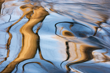 Summer landscape captured with motion blur of a rapids on the Rabbit River with abstract reflections of trees in calm water, Michigan, USA