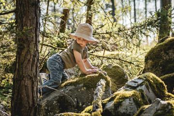 Cute infant boy adventurer playing in the woods in summer