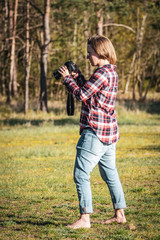 Young female photographer checking photos on her camera outdoors in the woods in warm eventing light