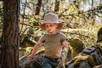 Cute infant boy adventurer playing in the woods in summer in warm evening light