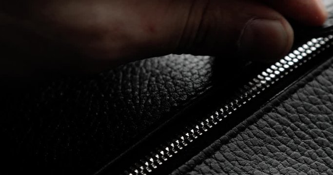 Testing metal zipper zips and unzips it on leather bag, man's hand closeup. Macro shot of unzipping and zipping metallic zipper on black leather accessory with guy's hand. Expensive brutal accessory.