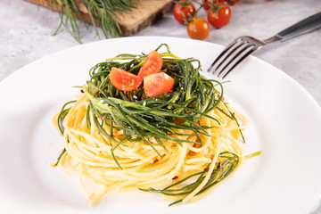 Spaghetti with agretti, a spring vegetable from Italy, and and ingredients and fork on a white...