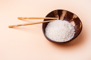 Coconut plate with rice and Chinese chopsticks on a pastel peach background. Asian food