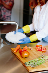 Obraz na płótnie Canvas Vertical photo of a woman with gloves washing a plate with water in a kitchen