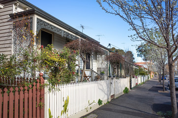 A row of weatherboard houses with 
Victorian-era wrought iron lacework and wooden fence in an Australian suburb.