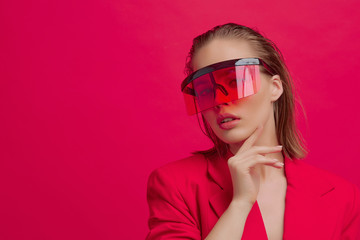 A cool stylish girl with a fashionable hairstyle and stylish glasses with a large glass poses on a bright red background