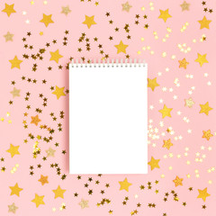 Notepad mockup on a pink pastel background with scattered gold stars confetti. Holidays concept.