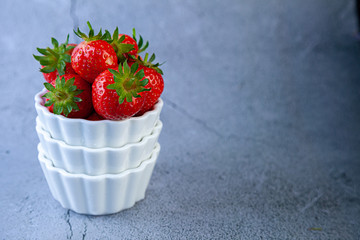 Strawberry berries in a white bowl on a concrete table. Place for text. Strawberries in a plate - dessert. Healthy food. Breakfast on grey background
