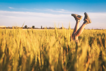 Girl lies in the field with her legs up in sneakers. Legs stick out in the field on blue sky background on sunset. The concept of leisure happiness. Selective focus, extremely shallow DOF.