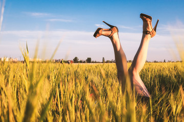 Girl lies in the field with her legs up in shoes on high heels. Legs stick out in the field on blue sky background on sunset. The concept of leisure happiness. Selective focus, extremely shallow DOF.