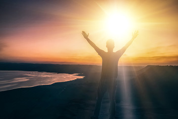 Fototapeta premium Silhouette of a man raising his hand to receive light on the top of the hill, freedom, travel, christian worship, concept success and win.