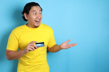 man holds credit card, smiling and pointing to the side, copy space