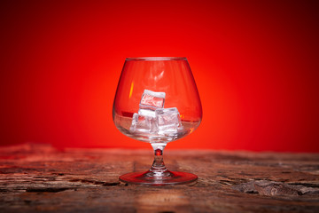 Empty whiskey or brandy glass with ice on a red background