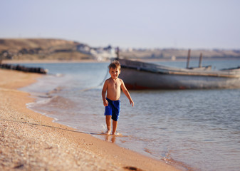 Fototapeta na wymiar a boy runs on the beach near a boat
