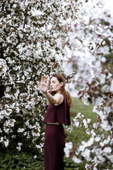 a beautiful brunette woman in a fashionable suit stands next to blooming Apple trees on a warm summer day. Stylish image for a walk in nature in the Park.