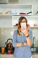 Modern young woman using cellphone in the kitchen.