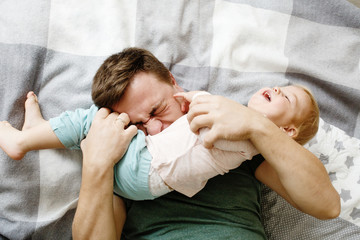 Top view of affectionate young father holding his baby daughter kid and tickling her