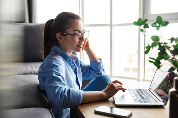 Image of pleased woman working with laptop and smiling while sitting