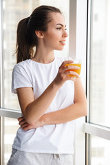Image of pleased woman smiling and drinking fresh juice while standing