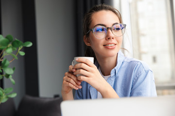 Image of woman drinking tea and working with laptop while sitting at table