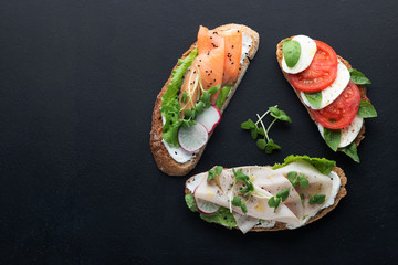 sandwiches with ham, radish, romano salad, baby basil, mascarpone cheese, caprese salad on a black background.