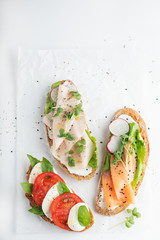 sandwiches with ham, radish, romano salad, baby basil, mascarpone cheese, caprese salad on a white background. copy space. top view.