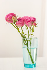 a sprig of spray roses in a glass on a table with perfume