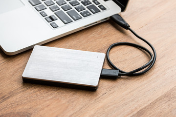 External hard drive connect to laptop computer on wooden background