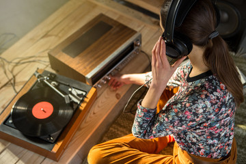 Young Woman listening a music on a HiFi system with turntable, amplifier, headphones and lp vinyl...