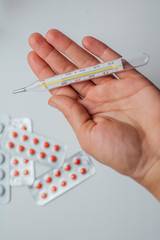 medical thermometer in hand on the background of a first aid kit and various pills