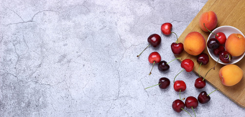 Fresh ripe cherries, cherries and apricots on a wooden board. Choosing healthy vegetarian food, concept of detox or diet. Fruit horizontal banner, light gray background, space for text.