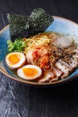 Asian noodle soup, ramen with pork, tofu, kimchi, vegetables and egg in blue bowl. Slate background. Top view. Bowl of asian style soup. Japanese cuisine. Top view. Banner. Asian food