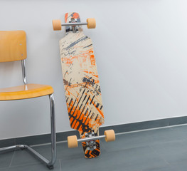 A drop through longboard skateboard is leaning against a white wall next to a wooden cantilever...