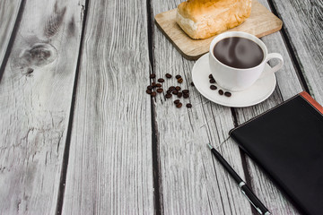 Black coffee, bread, workbook, pen on the table, white wood background With free space.